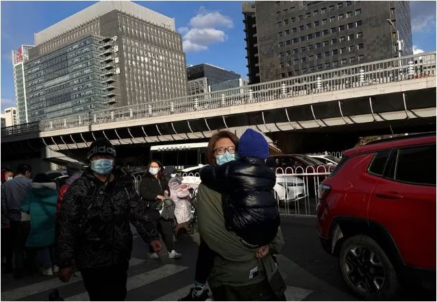 27 نوامبر 2023، زنی که کودکی را حمل می‌کند در خارج از بیمارستان کودکان در پکن، چین راه می‌رود.